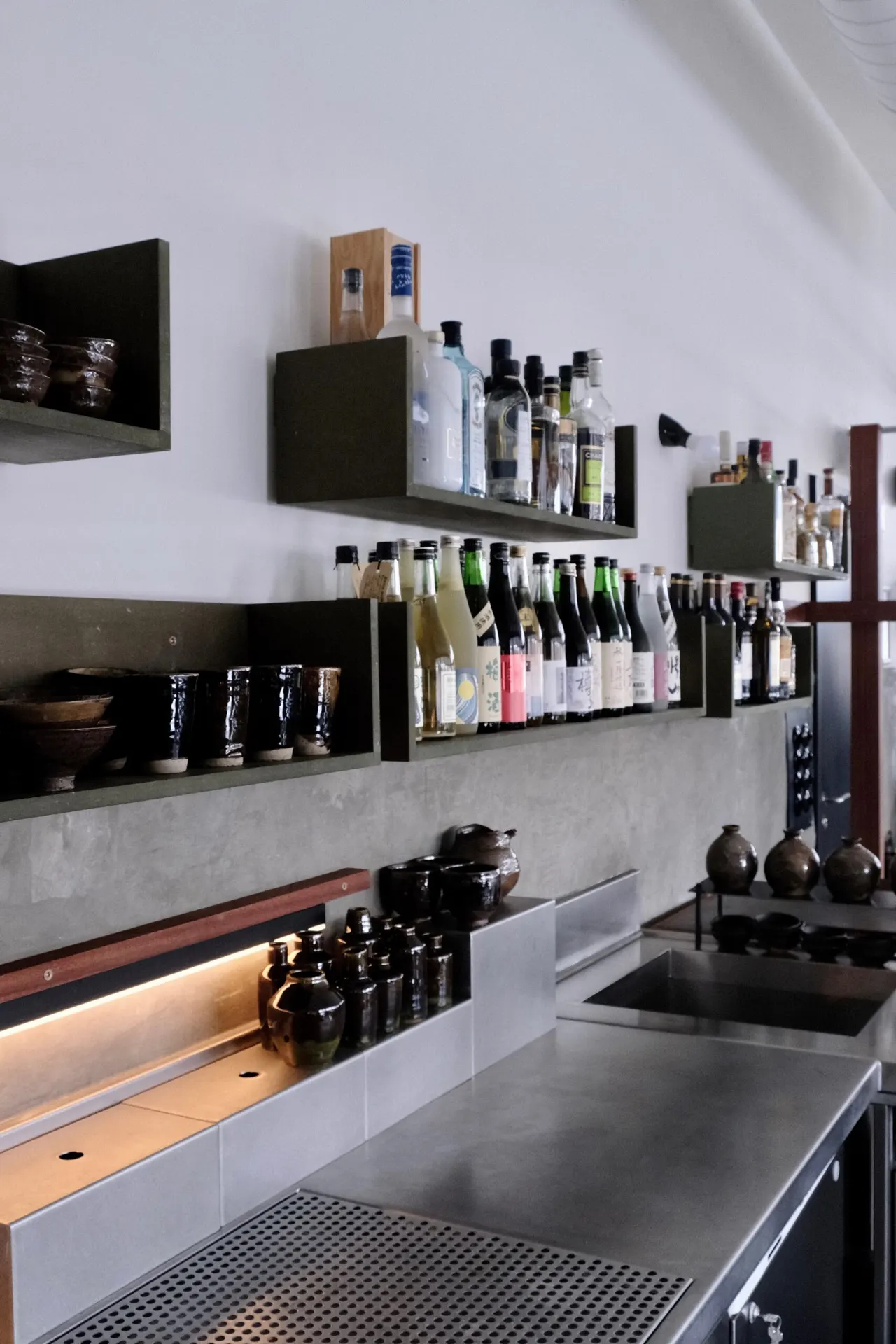 Open wandschappen met flessen boven een inox werkblad