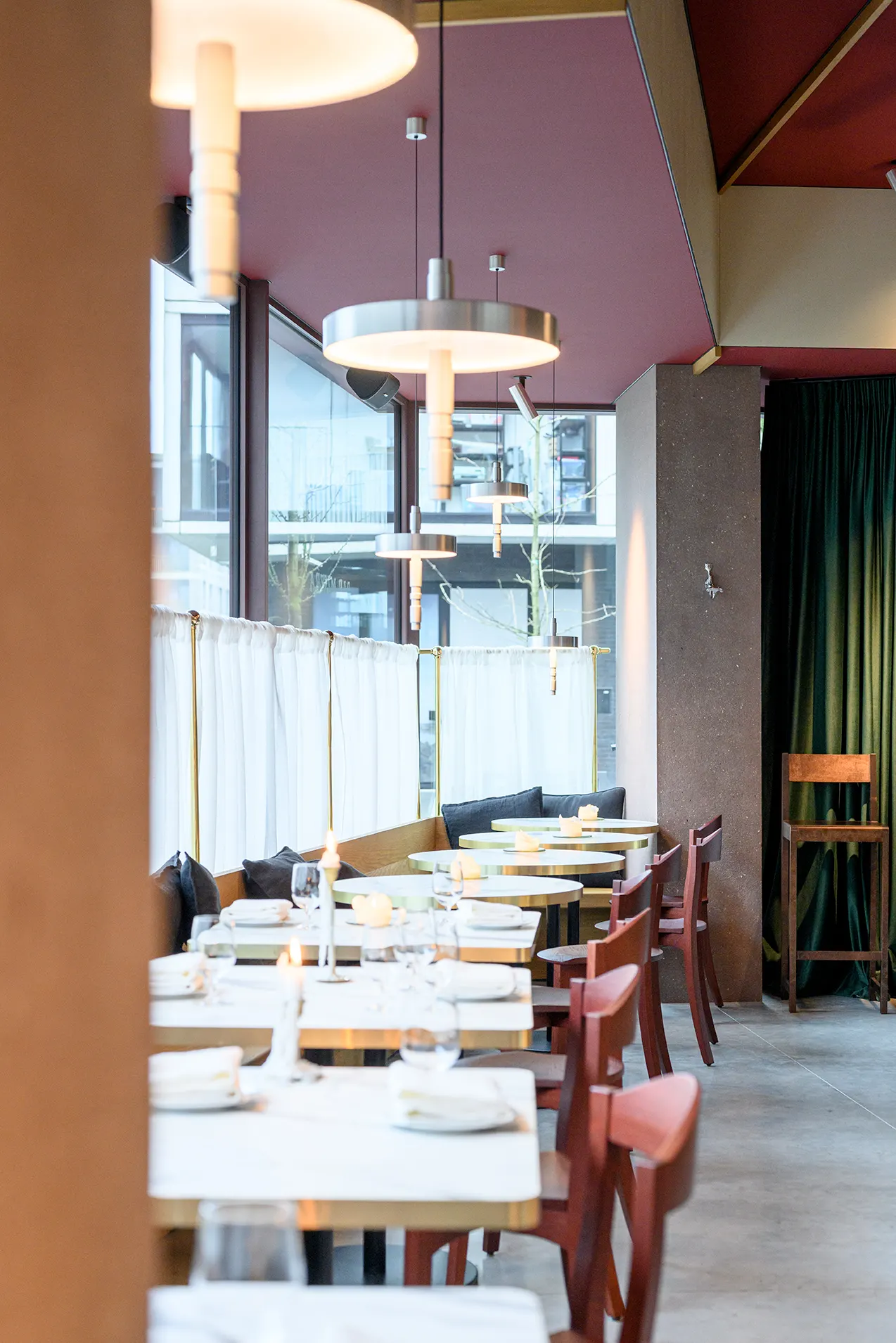 Rij bistrotafels langs de ramen onder een bordeauxrood plafond