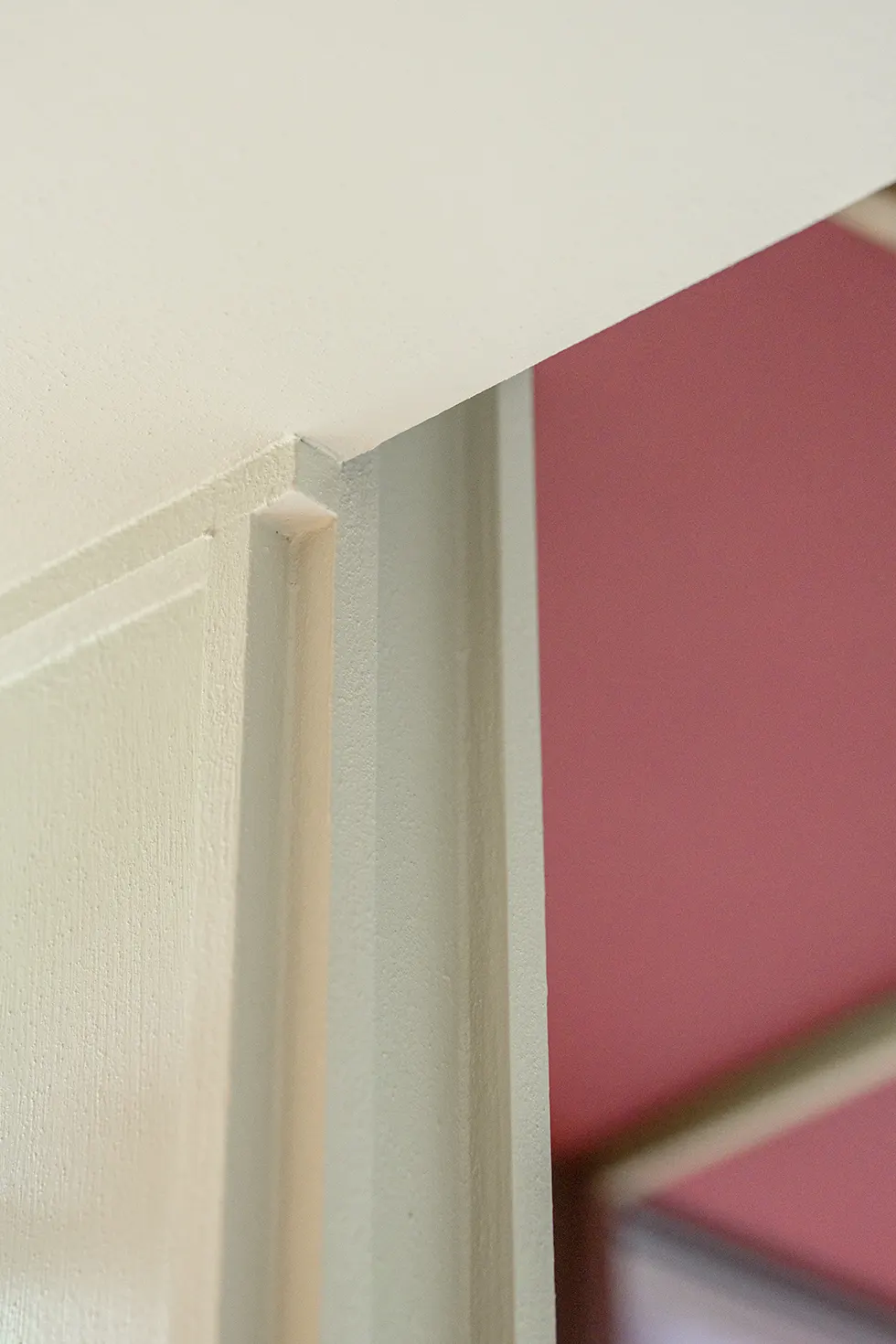 Detail van een eiken lijst tegen een bordeauxrode wand
