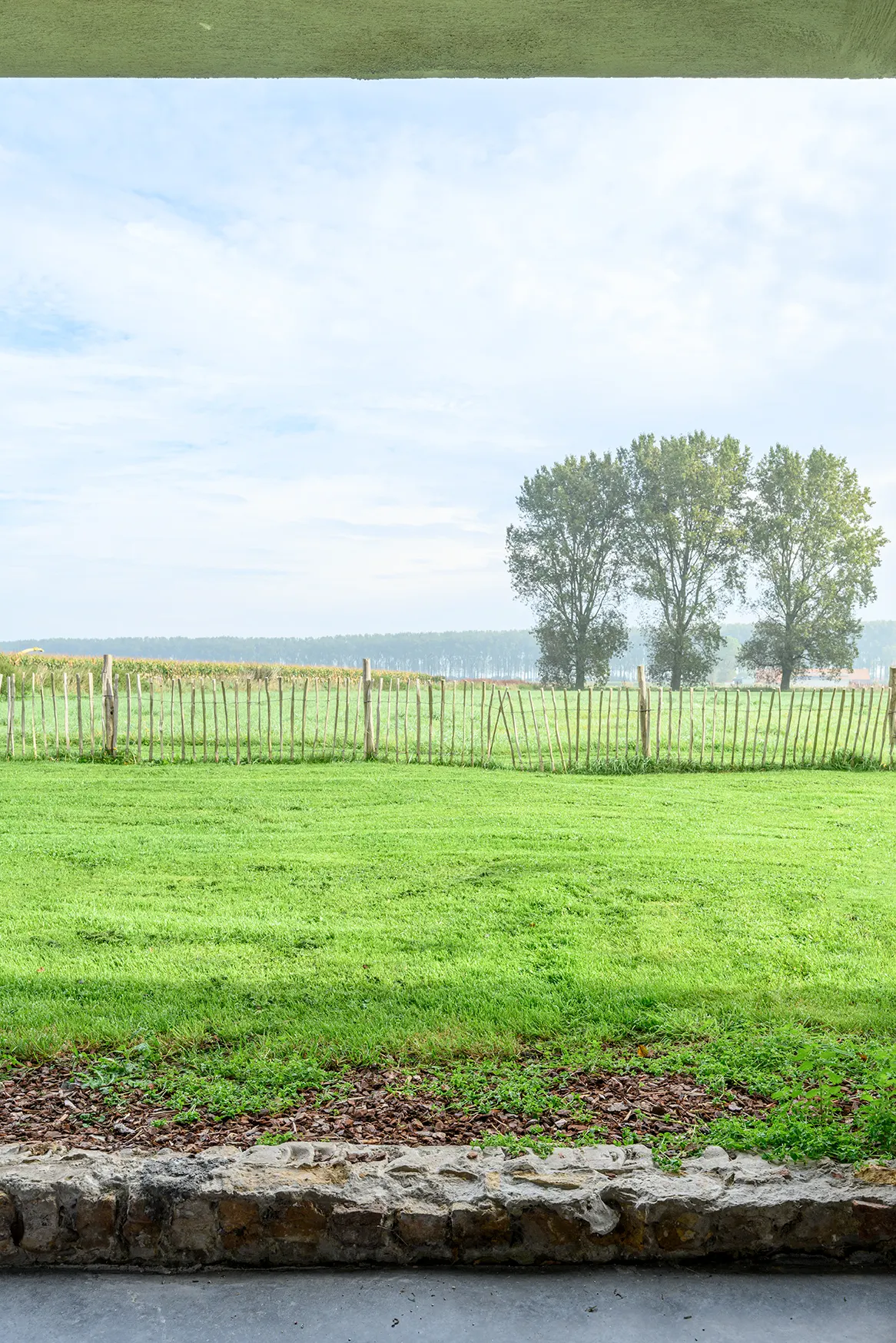 Zicht vanuit een kamer op weiland en bomen in de polder bij Dudzele