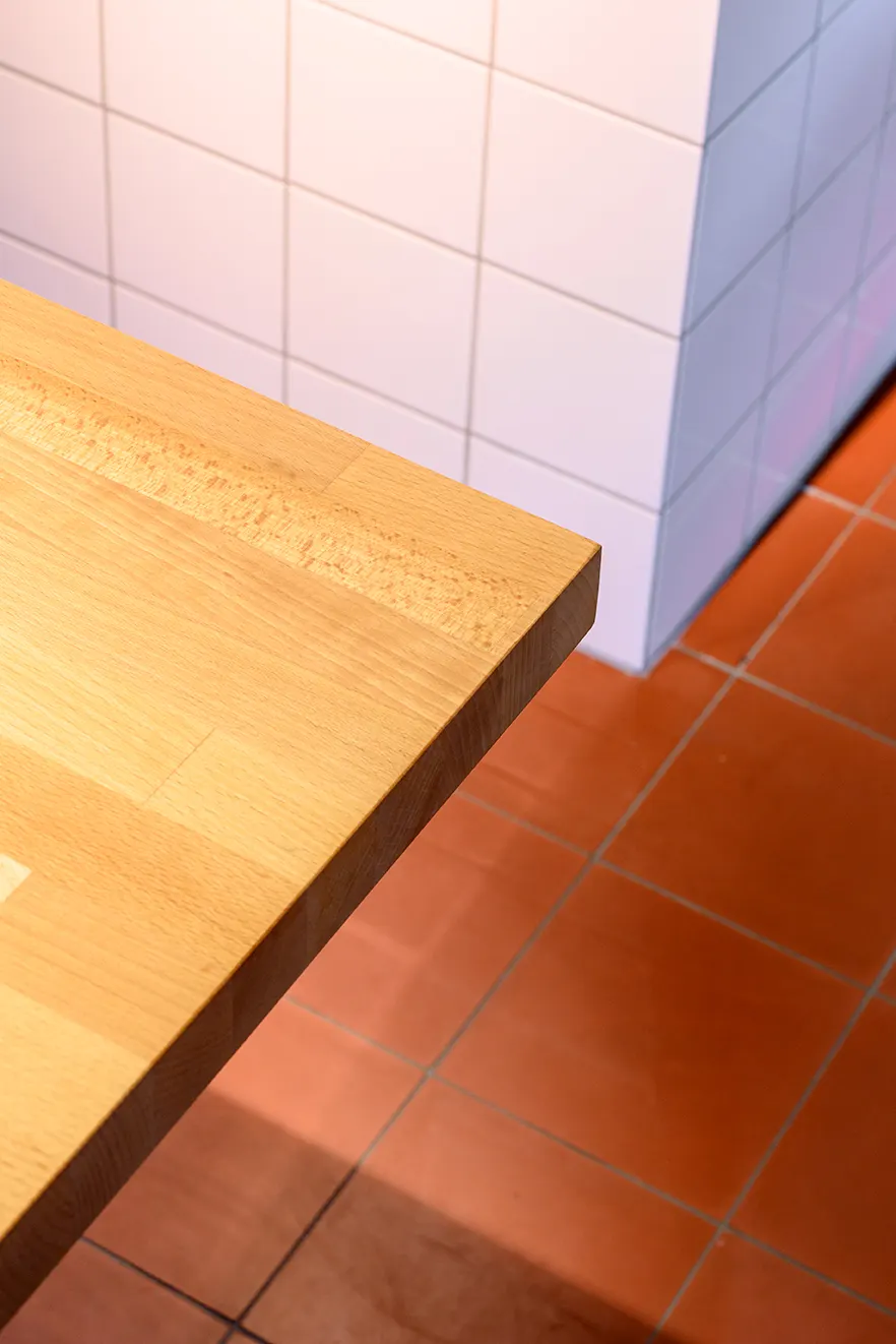 Hoek van een tafel in massieve beuk tegen witte tegels bij Carcasse Knokke
