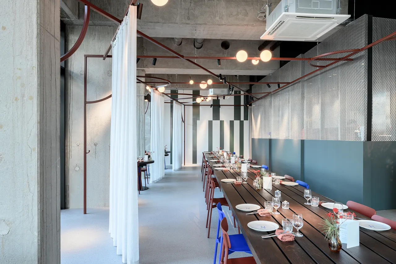 Lange tafel met rode stoelen onder de bordeauxrode staalstructuur van l'Abbiocco in Knokke