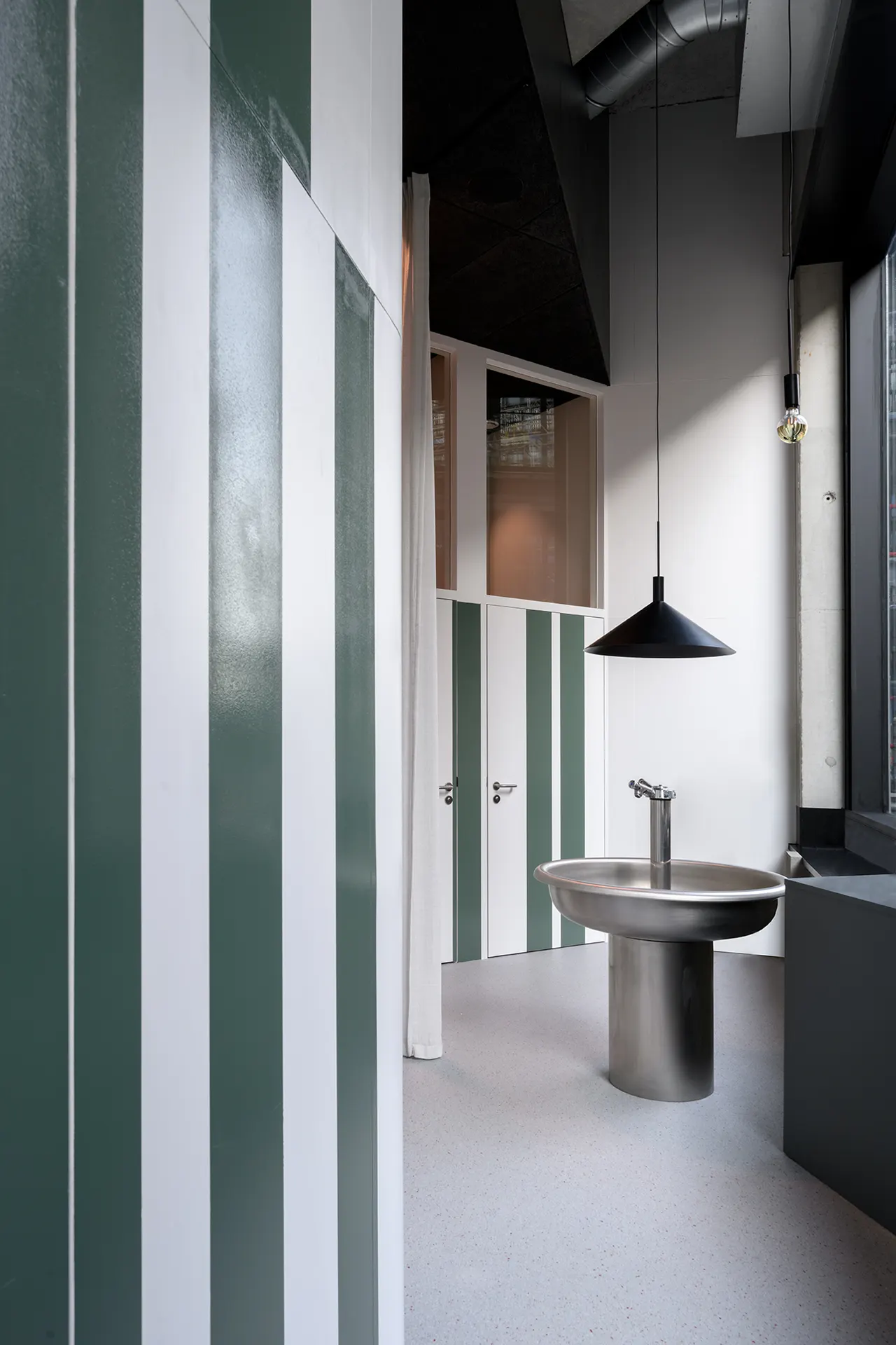 Groen gestreepte wand met inox wastafel en zwarte hanglamp