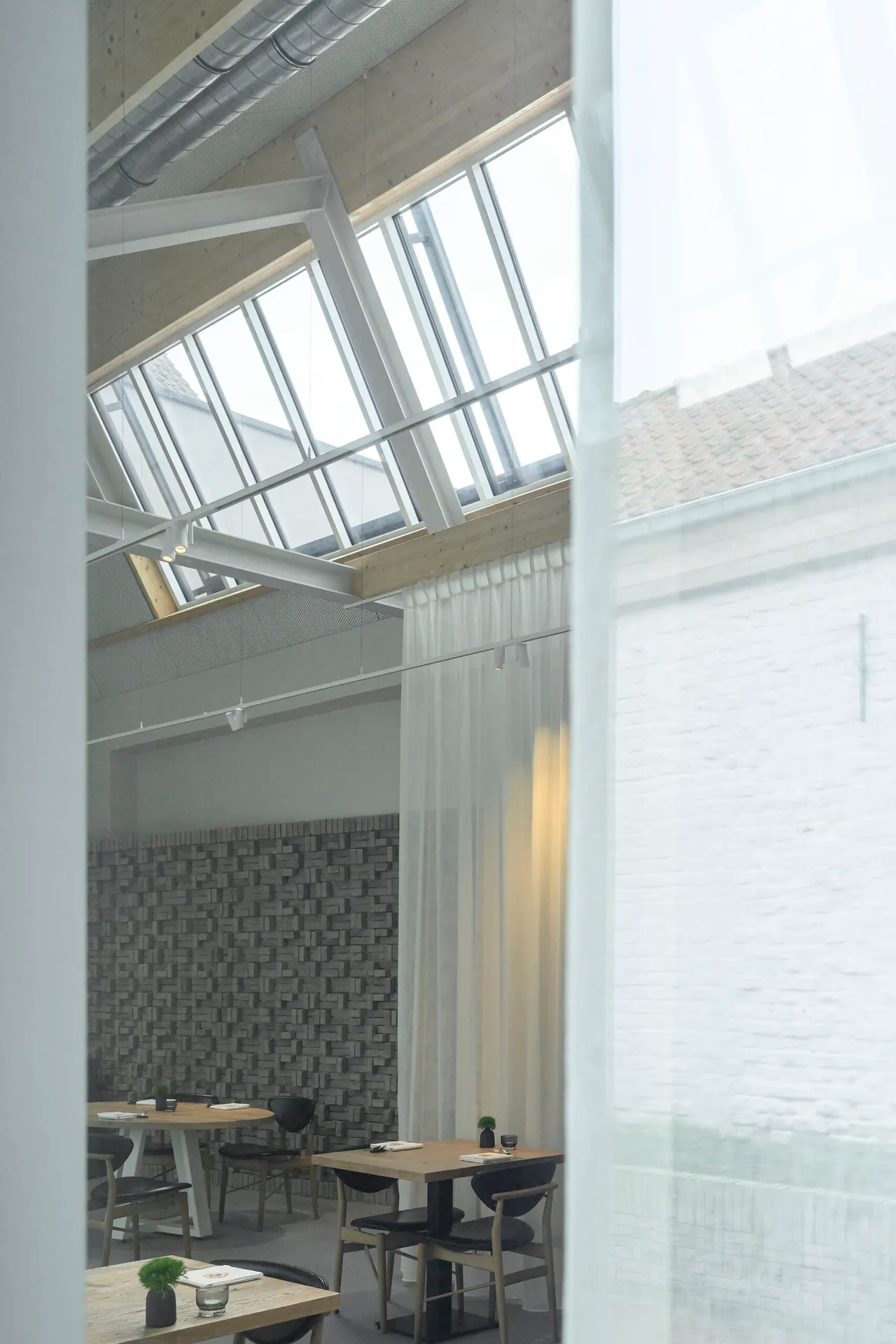 Zicht door een gordijn op de zaal en de dakramen van M-Bistro in Nieuwpoort