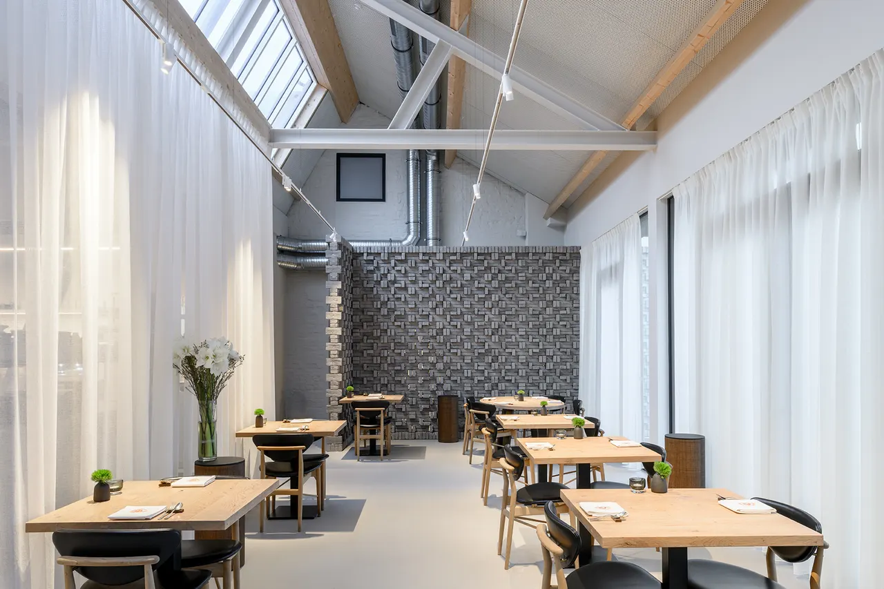 Restaurantzaal van M-Bistro in Nieuwpoort met houten tafels, witte gordijnen en dakramen