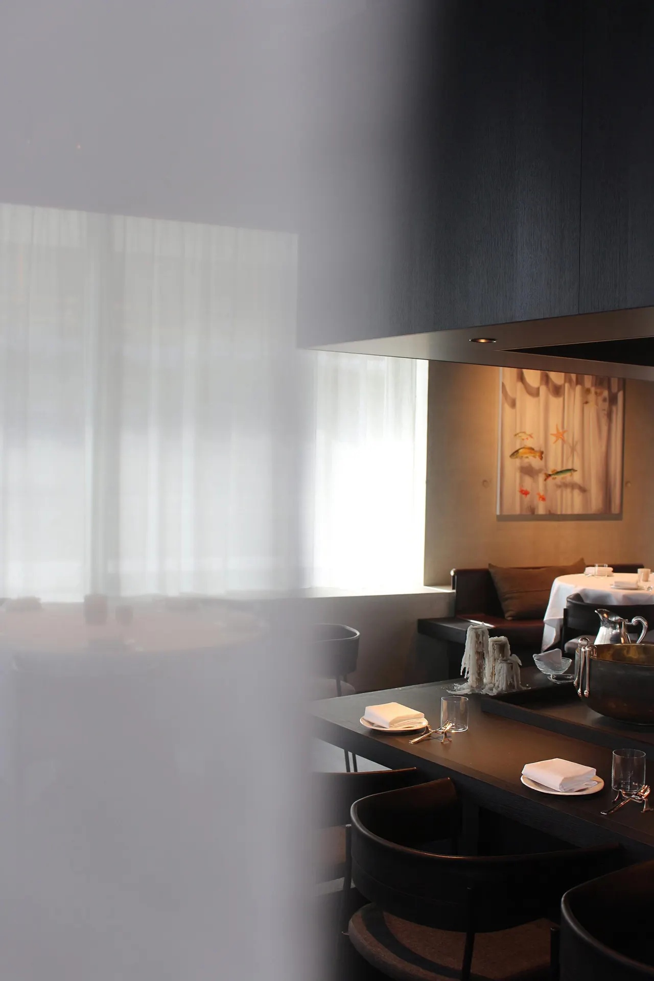 Donkere zaal van restaurant Misera in Antwerpen met wit gordijn en tafels