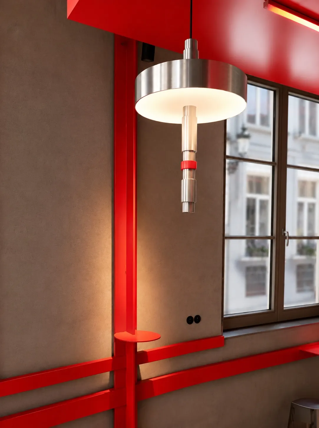 Felrode stalen kolom met aluminium hanglamp bij de ramen van Mosh!