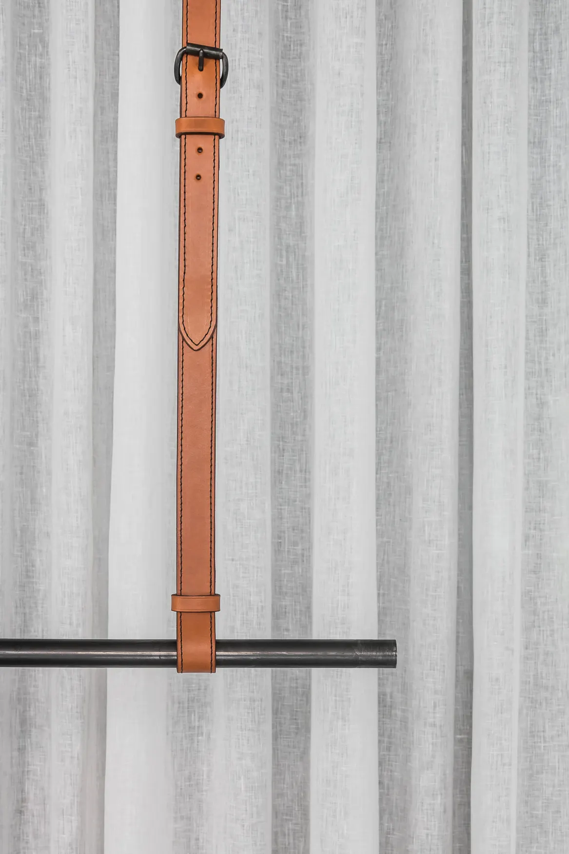 Lederen riem die een kledingrek ophangt tegen een linnen voile bij Six Edges
