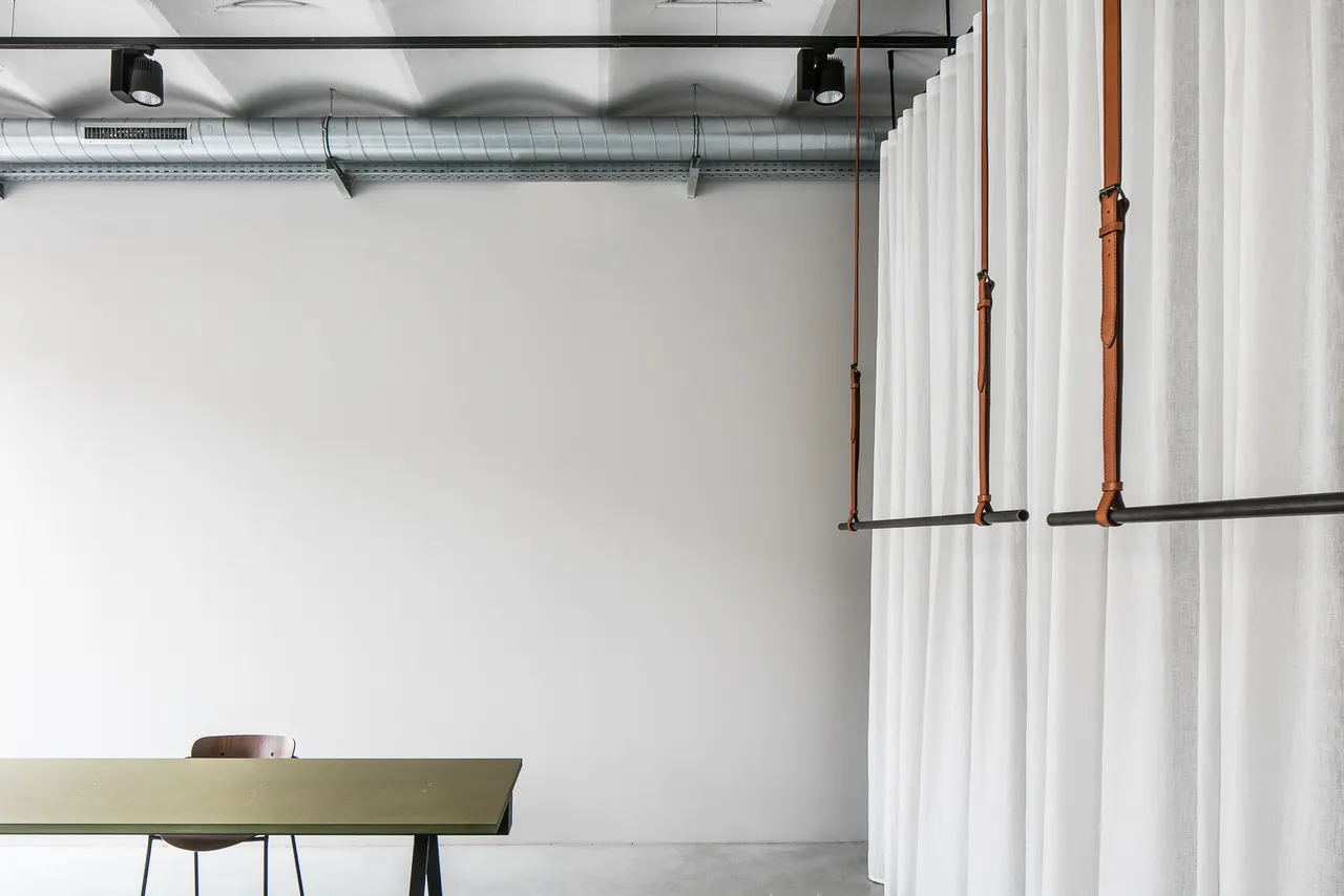 Olijfgroene tafel en kledingrek in de witte showroom van Six Edges in Gent