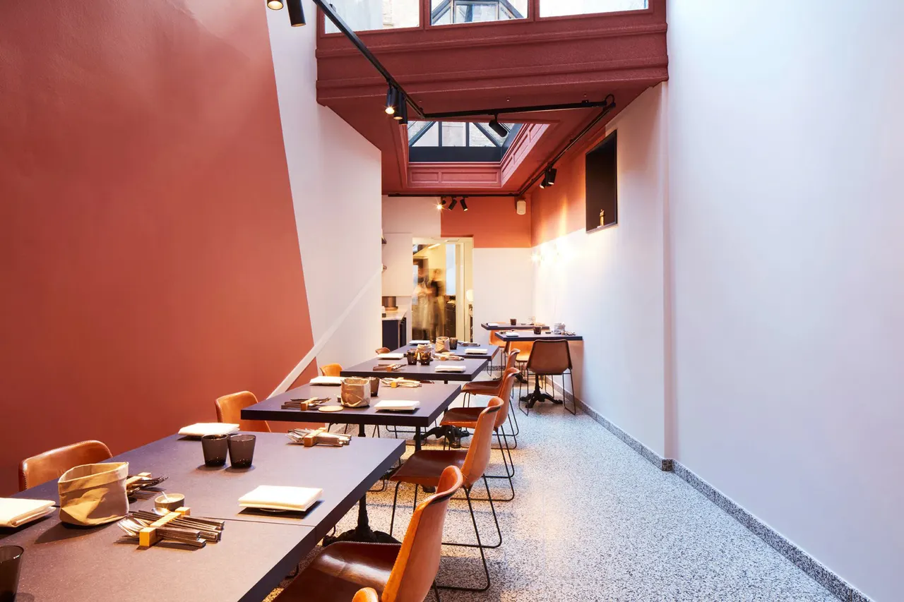 Lange eetzaal van restaurant Souvenir in Gent met schuine terracotta kleurvlakken en glazen dak